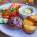 A well-presented gourmet meal featuring grilled patty, potatoes, and fresh vegetables.